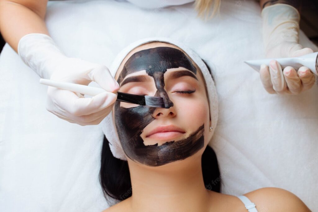 cosmetologist-applying-black-mask-pretty-woman-face-wearing-black-gloves-gorgeous-woman-spa_361821-1061
